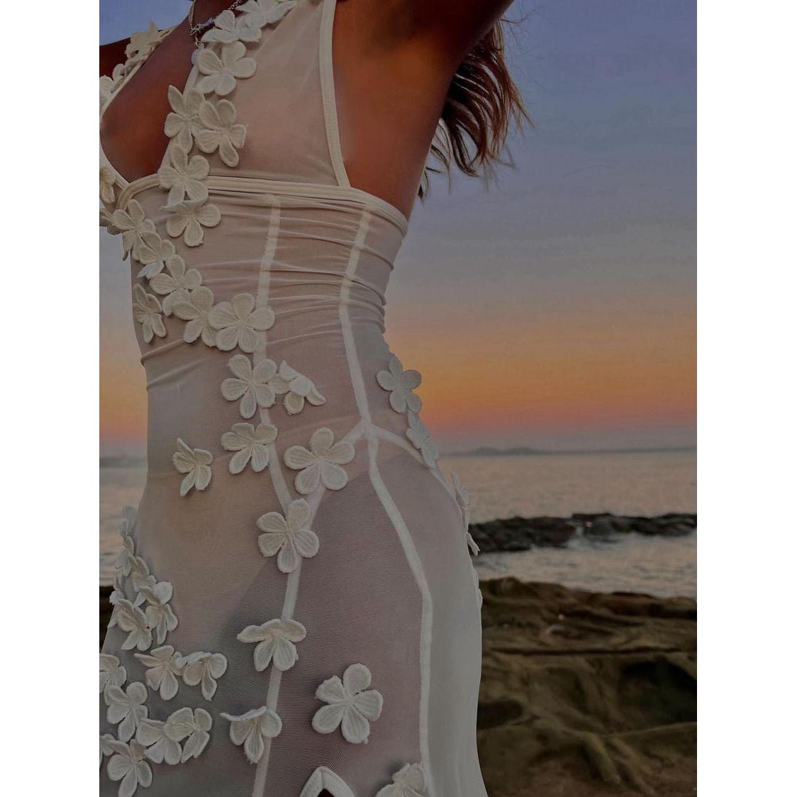 Marcia Maxi in White, Size S/8. Featuring a sheer design with small 3D white flowers placed over the dress with a semi low cut bust and high mid thigh side split. Comes with an optional slip that makes the dress less sheer. Stunning for events where you want to stand out or a nice date outfit. Featuring a form fitting top area where it slowly flows out around the legs. Up close view of dress.