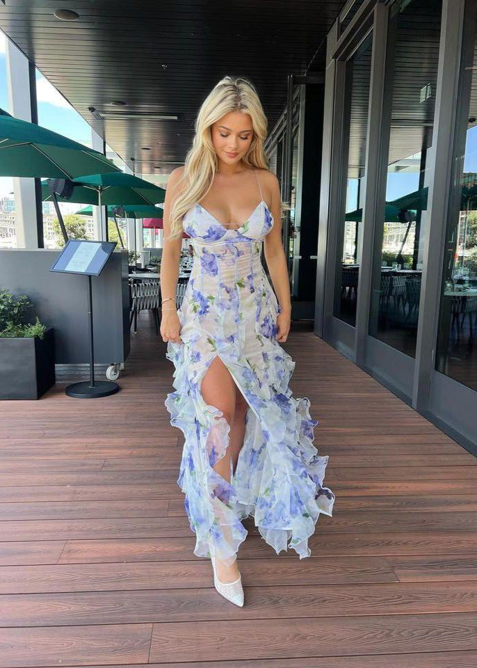 Menti Iris Maxi in Blue Floral is all the way from Greece, Size M. Main colour is semi sheer white with floral patterns of purple/blue with a double lined bust and thin straps. This dress has gorgeoys frills going vertically from hip height to bottom of the dress. It features a mid thigh split for easy movement and is tight fitting on bust/torso when it then starts to flow out. Perfect for formals, races, wineries, birthdays, bottomless brunches etc. Front on full lenght of dress.