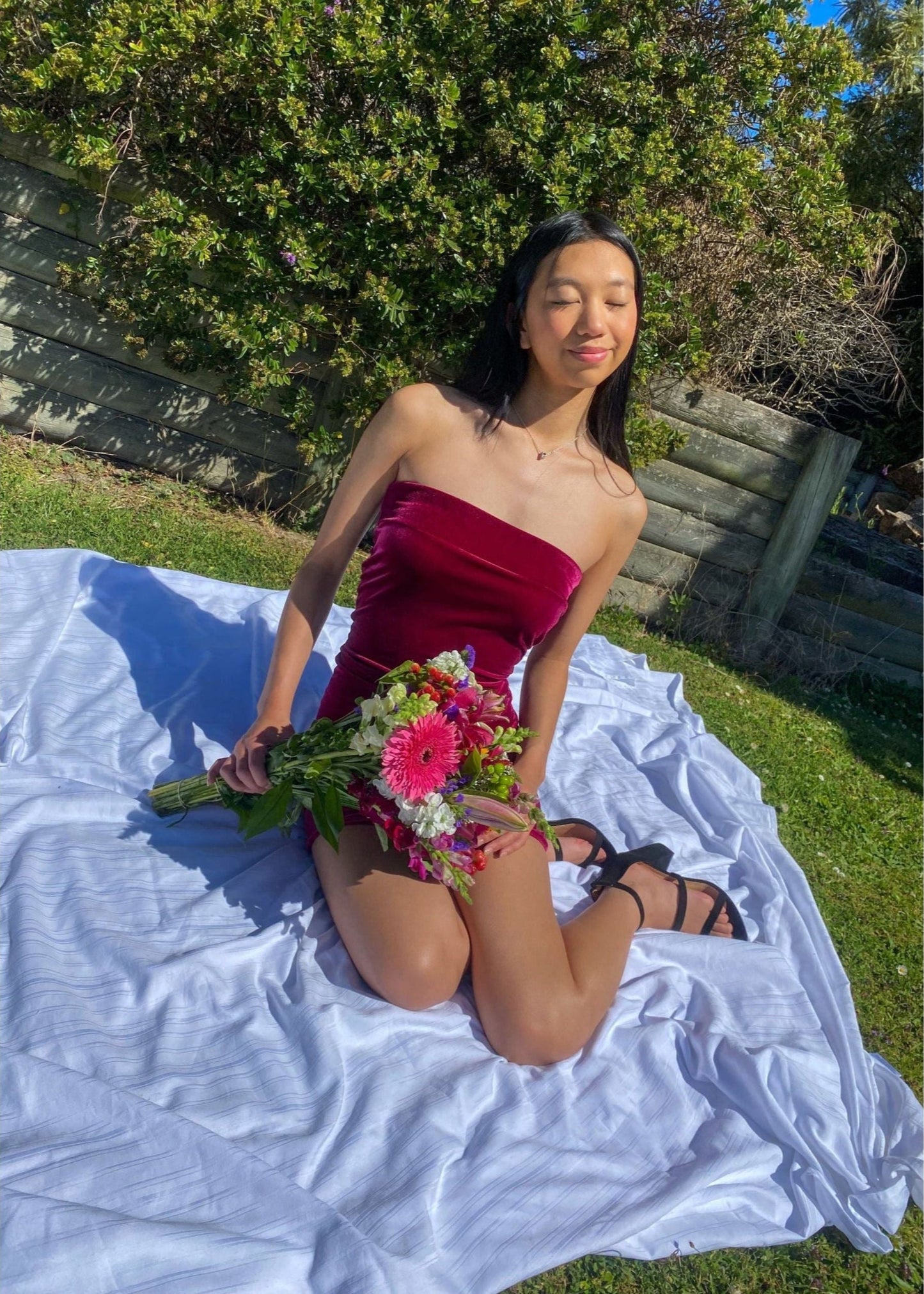 7th and York Strapless Mini Dress in Magenta, Velvet Material. Perfect for events like the races, birthdays etc. Size 6/XS dress. Sitting down view of dress outside, front of dress slightly covered by flowers