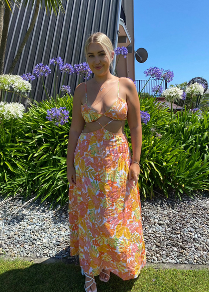 Issy Citrus Aloha Maxi in Floral Print with White, Orange, Pink and Yellow with small hints of green, Size 14. Featuring a lace up back bust area with a open back below with zip on skirt area. Front has stomach cut out with two small straps to attach bust and torso section of dress. Perfect for races, wineries, bottomless brunches etc. Front on full length view of dress.