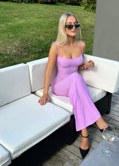 SKIMS Long Slip Dress in Petal Pink, Size XS and M. Featuring a body hugging fit, straight neck and adjustable spaghetti straps. Can be dressed up or down. Dress can appear semi sheer depending on how much it is stretched when on. Can be dressed up or down. Front on sitting down view of dress.