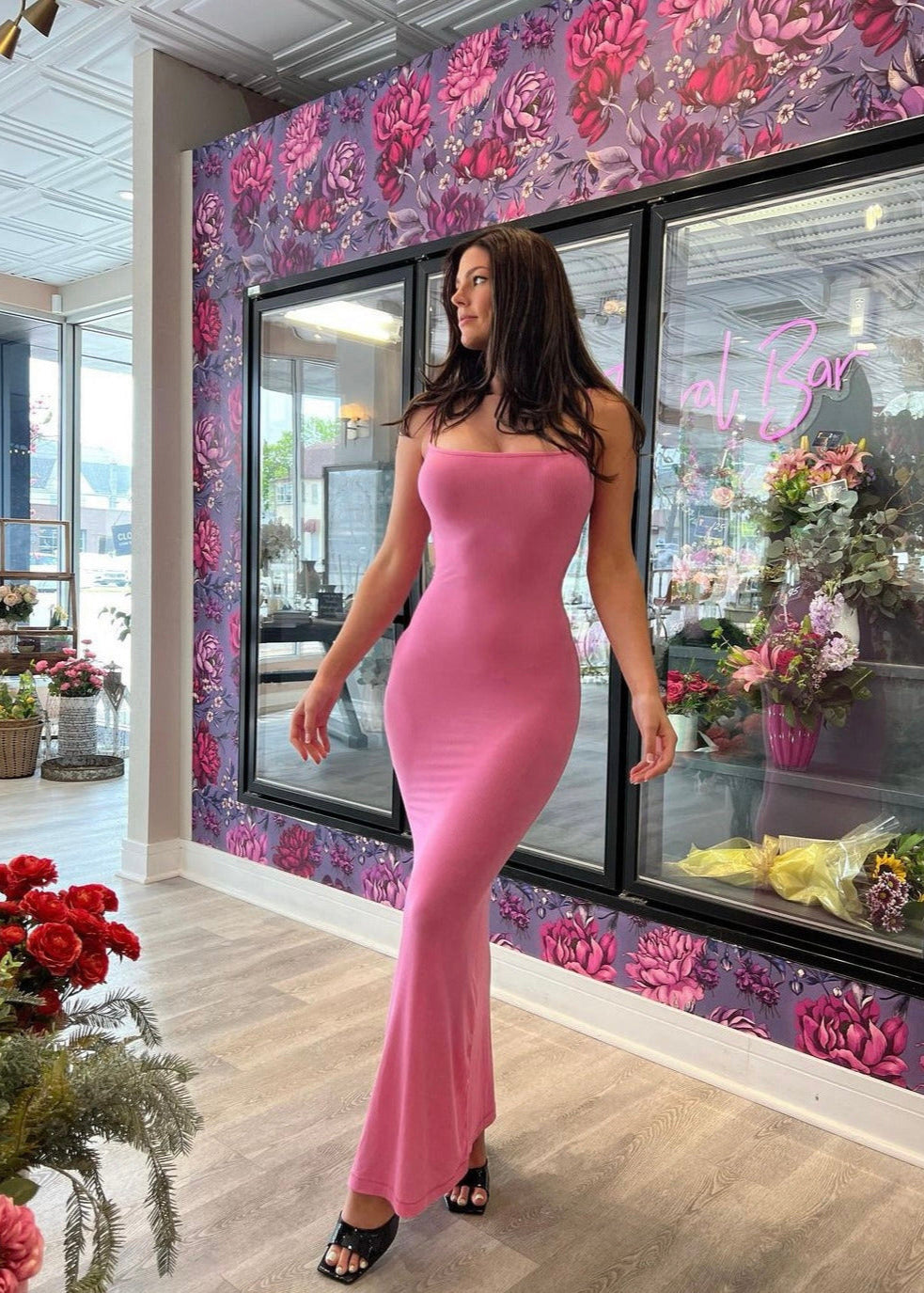SKIMS Long Slip Dress in Bubblegum Pink, Size M. Featuring a body hugging fit, straight neck and adjustable spaghetti straps. Can be dressed up or down. Dress can appear semi sheer depending on how much it is stretched when on. Can be dressed up or down. Front on full length view of dress.