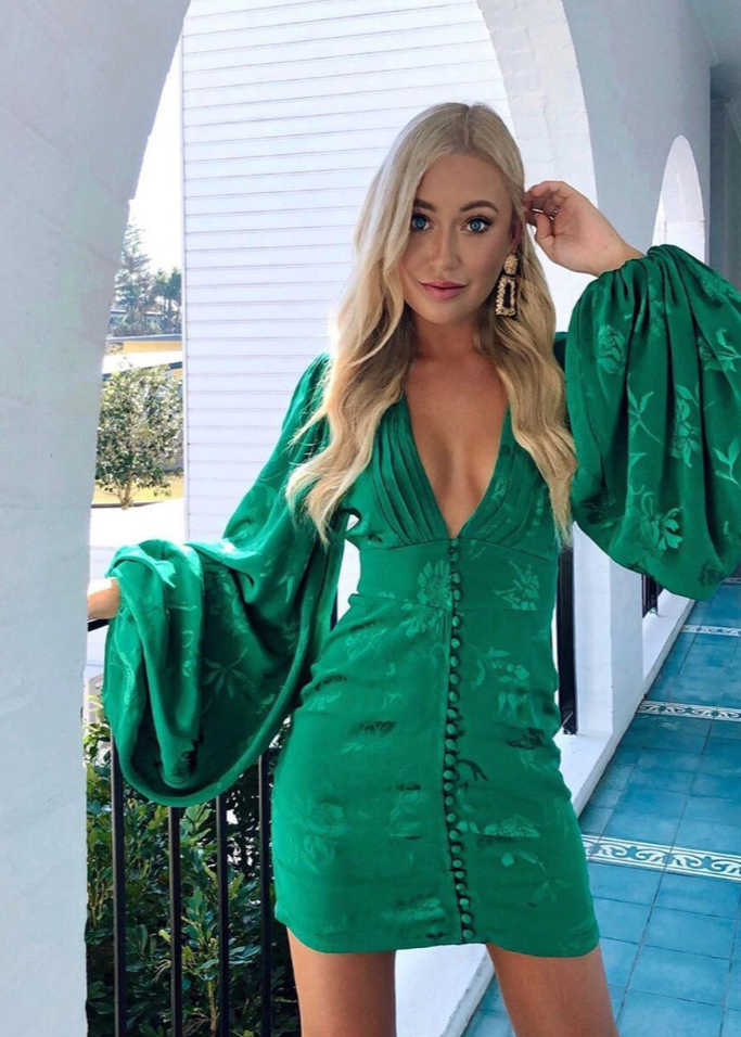 Rat and Boa Isabella Mini Dress in Green, Size S. Featuring balloon sleeves and a deep v neck with a buttoned front and zip up back. Additionally it features some floral designs in green that give off a slight shine to make it stand out against the green fabric. Perfect for parties, bottomless brunches etc. Front of view of dress.